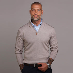 A smiling man with a shaved head and trimmed beard wears the COLLARS AND CO Oatmeal Cashmere Touch Australian Merino Quarter Zip Sweater over a blue checkered shirt, posing against a plain gray background.