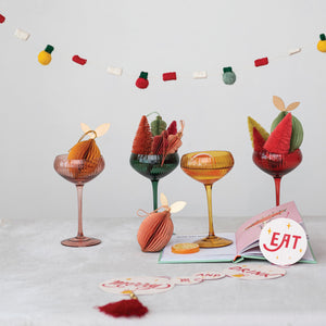 Four CREATIVE COOP STEMMED CHAMPAGNE GLASSES, each ribbed with a round stem in green, pink, red, and yellow, are lined up against a white background.