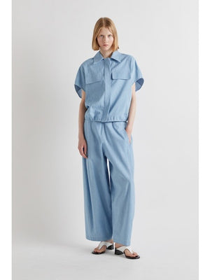 Model wears MEIMEIJ - DRAWSTRING COTTON PANTS in light blue, featuring a loose fit, wide legs, cropped ankle, and drawstring waist. Styled with white sandals. Image shows shoulders to feet against a plain background.