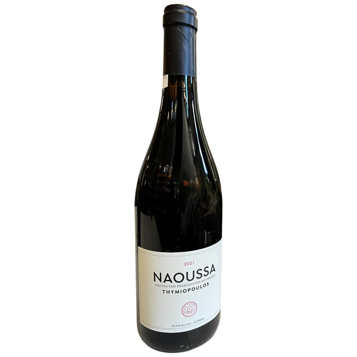 A bottle of THYMIOPOULOS ‘NAOUSSA’ XINOMAVRO 2021 red wine with a white label, standing on a white table in a restaurant.