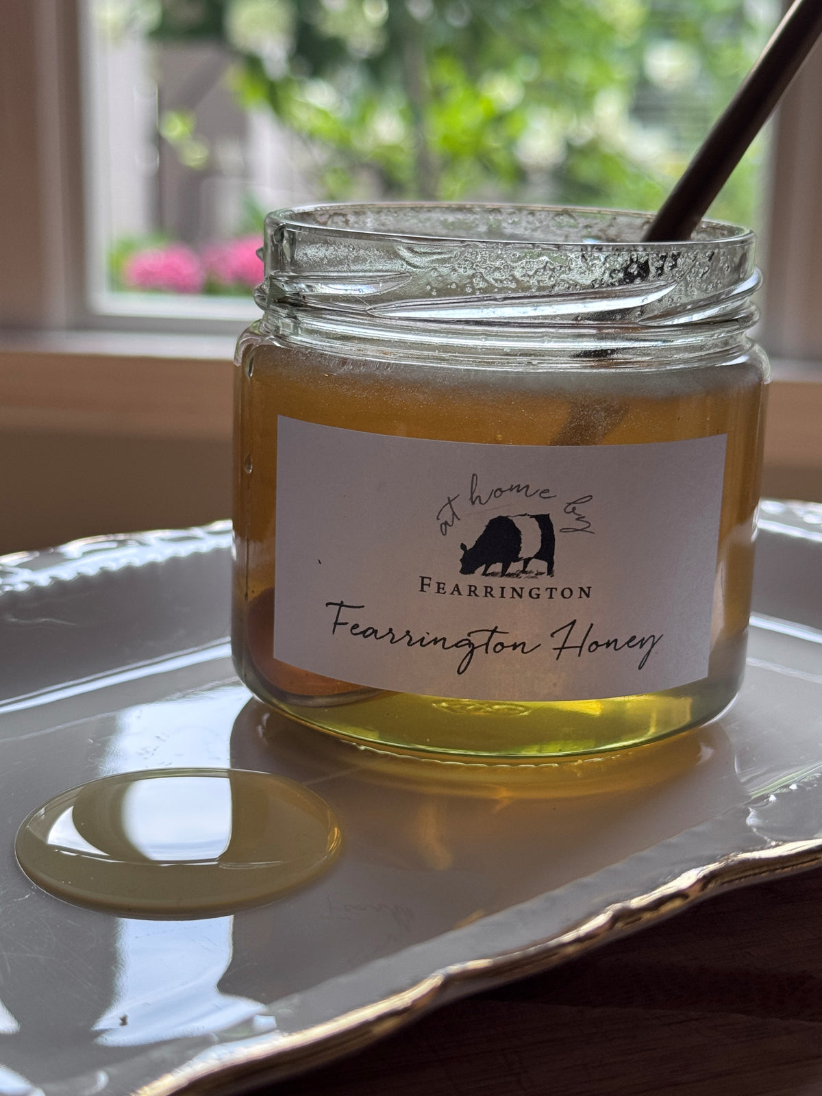 The Fearrington Signature Collection's hexagonal glass jar elegantly holds their Wildflower Honey, known for its raw quality. The label states: "Raw, Unfiltered. Handmade with care in our kitchens. May contain allergens. 282 grams, 10 oz." Inside is the finest golden honey from Fearrington House.