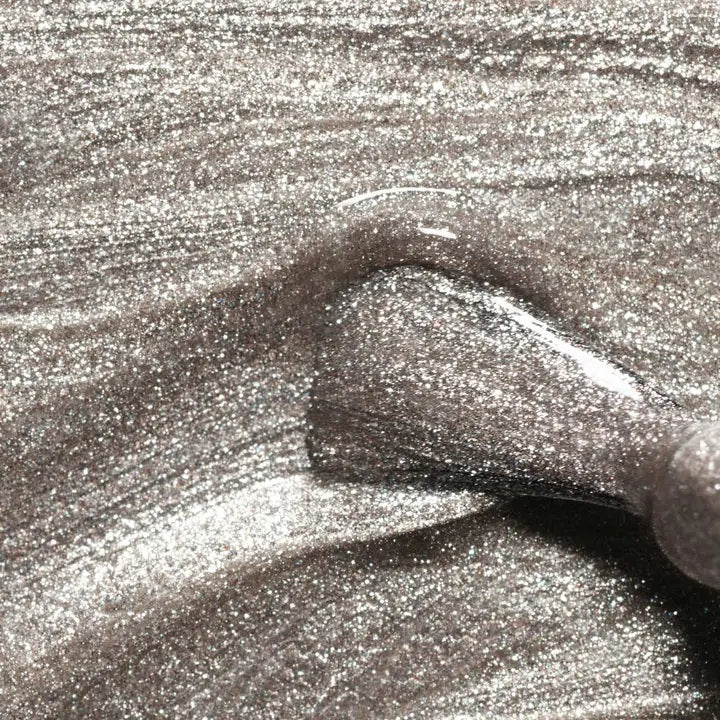 A transparent glass bottle of MANUCURIST - GREEN™ Nail Polish in Disco by MANUCURIST INC contains a sparkling silver glitter vegan polish. The bottle features a black cap and a white label adorned with green and black text.
