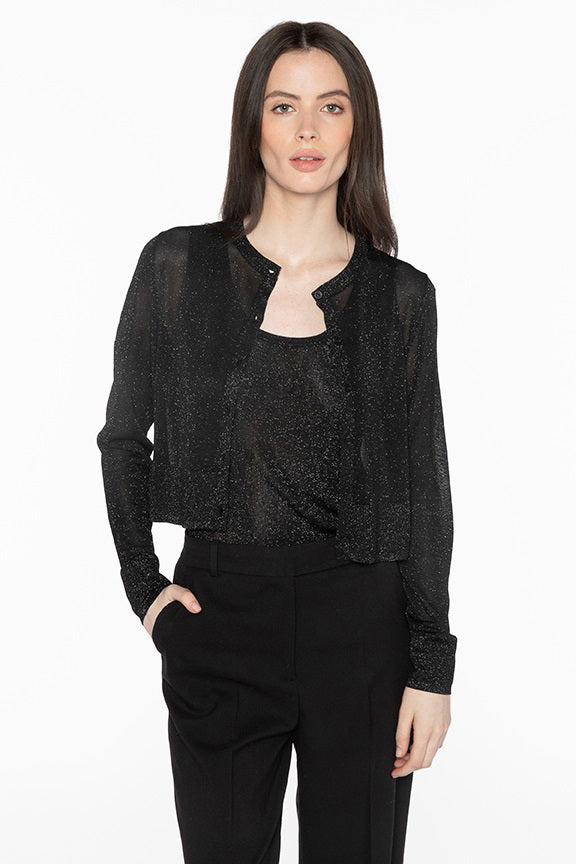 A woman with long, dark hair is wearing the KINROSS CASHMERE - SHIMMER CROP CARDIGAN from KINROSS over a black top and black pants. She has her right hand in her pocket and is posing against a plain white background.
