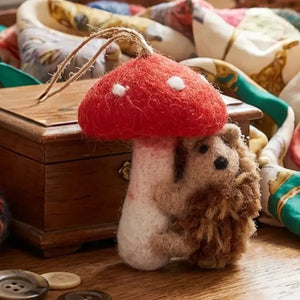 Handmade wool TOADSTOOL HEDGEHOD ORNAMENT featuring a hedgehog hugging a needle felted toadstool with a hanging loop.