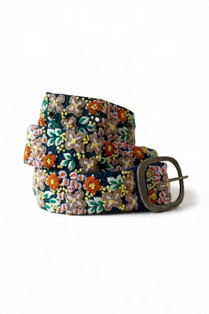 JENNY KRAUSS - MORNING DEW FLORAL EMBROIDERED WOOL BELT in dark blue wool with colorful floral embroidery and a silver-tone metal buckle, worn over blue jeans; this handcrafted Peruvian accessory highlights intricate needlework.