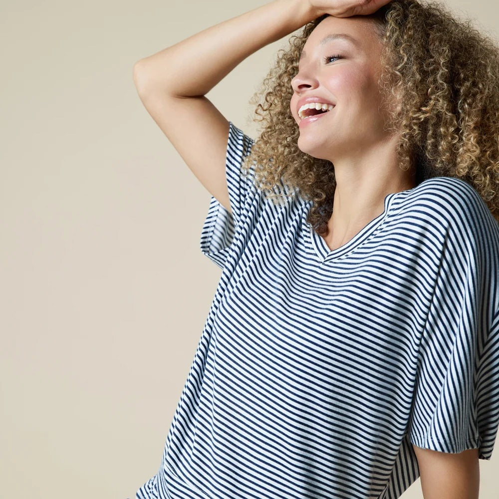 A woman wearing a light blue and white striped SOFTIES - DREAM RELAXED V-NECK WITH CAPRI LOUNGE SET with a V-neck, capri-length pants, and white sneakers.