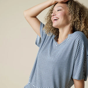 A woman wearing a light blue and white striped SOFTIES - DREAM RELAXED V-NECK WITH CAPRI LOUNGE SET with a V-neck, capri-length pants, and white sneakers.