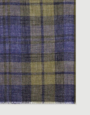 A young person with short dark hair wears a navy sweater and the HARTFORD Tartan Wool Scarf in Navy, Indigo, and Olive from HARTFORD, tied loosely around their neck, looking directly at the camera against a plain light background.