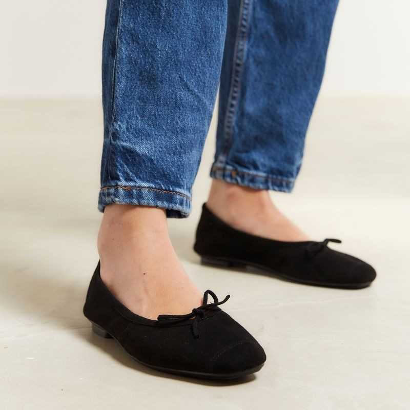 Wearing rolled-up blue jeans with REQINS - HARMONY SUEDE BALLERINA FLATS IN NOIR, featuring chic bow details—a timeless addition to any classic wardrobe.