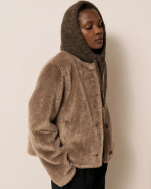 Wearing the HARTFORD MEVA Hood in Chocolate, a person gazes seriously at the camera against a plain background.
