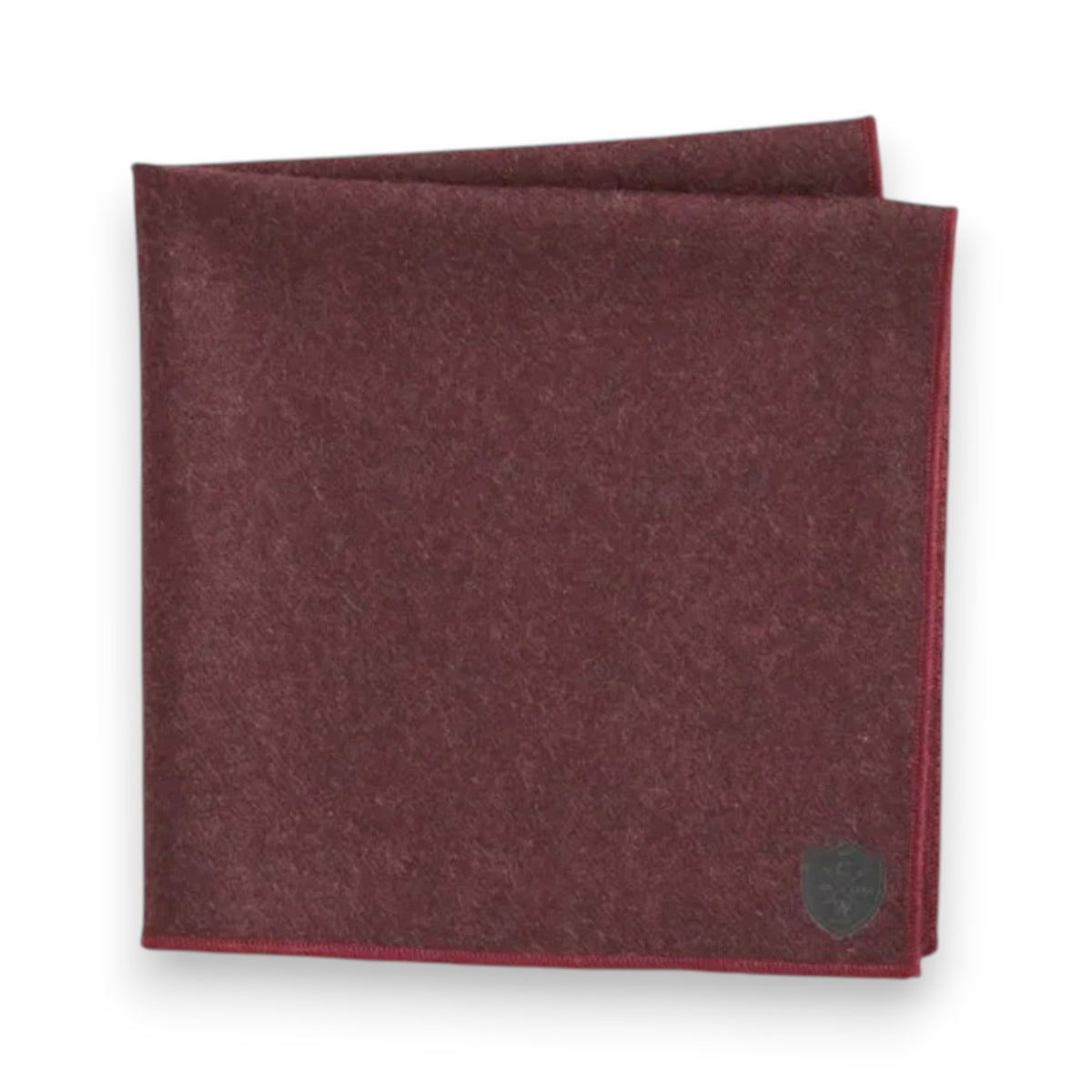 A neatly folded Clifton Wilson cashmere pocket square features a subtle stitched border and a small dark emblem in one corner, displayed on a white background.
