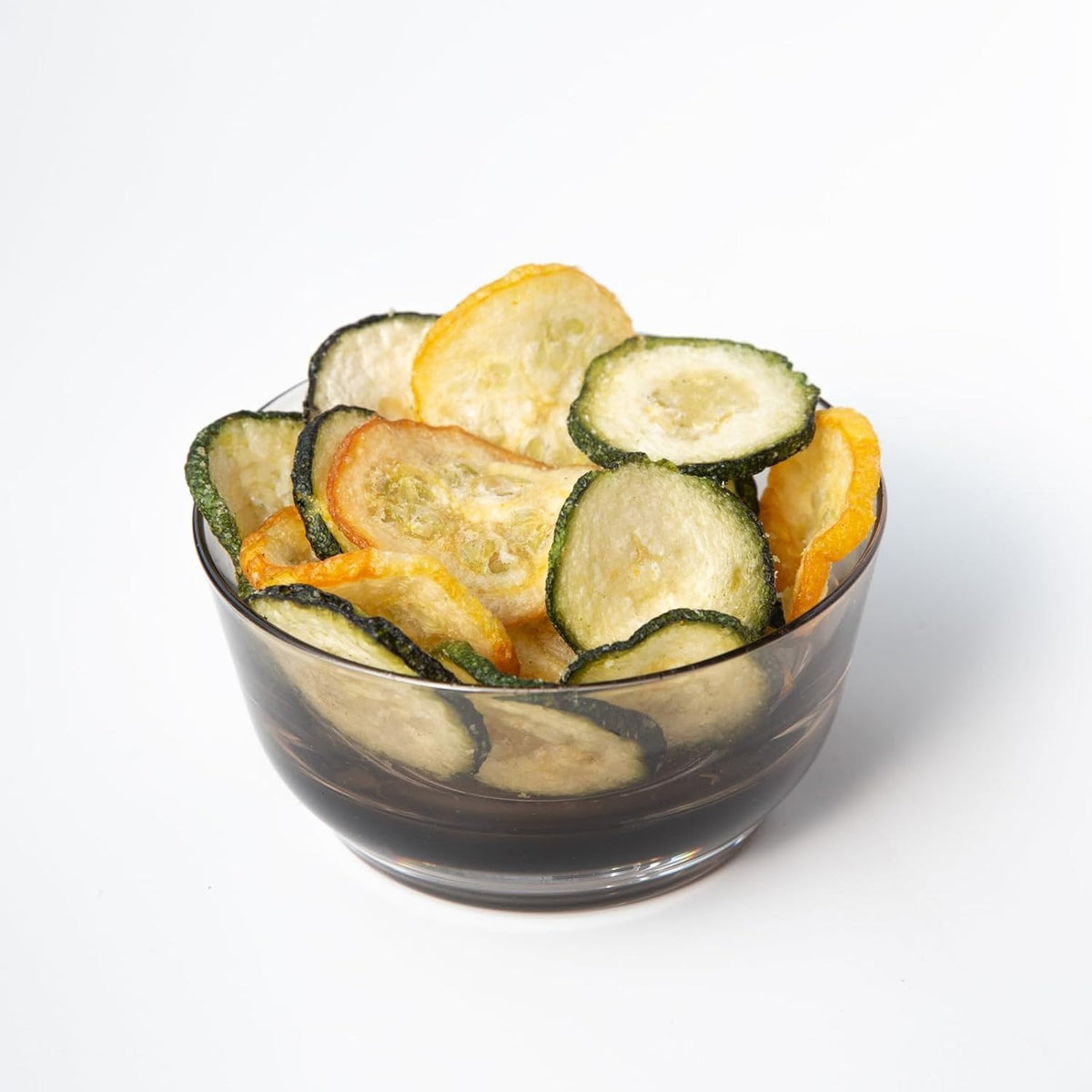 A graphic displays two zucchinis and zucchini slices with the text “approx. 2 lbs of fresh zucchini,” alongside a ROOT FOODS bag labeled “ROOT FOODS - ZUCCHINI CHIPS,” indicating that it takes about 2 lbs of fresh zucchini to make one bag of these tasty ROOT FOODS veggie chips.