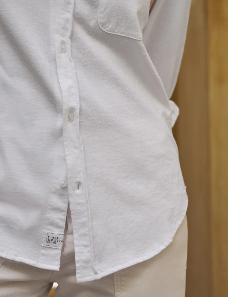 A woman with curly hair models the FRANK & EILEEN WAVERLY NYC Button Up Shirt in Vintage Jersey White, shown indoors from shoulders to waist, hand on hip, highlighting its classic chest pocket.
