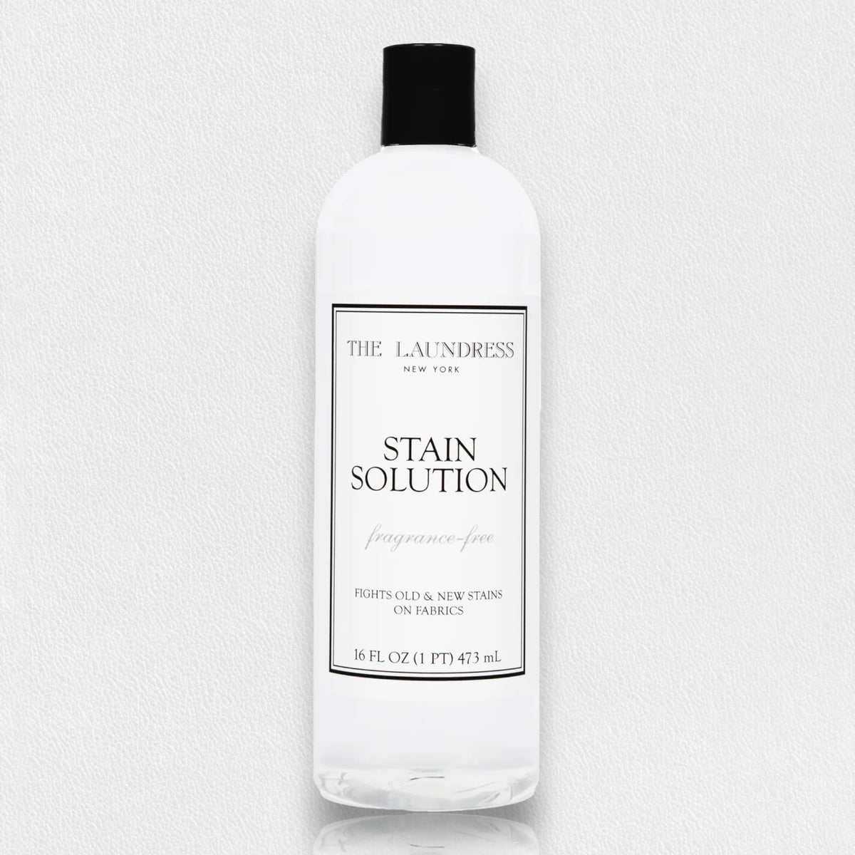 A bottle of THE LAUNDRESS - STAIN SOLUTION 16OZ is shown against a light background. The label reads &quot;The Laundress New York, Stain Solution, fragrance-free, Fights old &amp; new stains on fabrics.&quot; This powerful unscented solution comes in a 16 fl. oz. (1 pint) or 473 mL bottle.