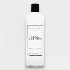 A bottle of THE LAUNDRESS - STAIN SOLUTION 16OZ is shown against a light background. The label reads "The Laundress New York, Stain Solution, fragrance-free, Fights old & new stains on fabrics." This powerful unscented solution comes in a 16 fl. oz. (1 pint) or 473 mL bottle.