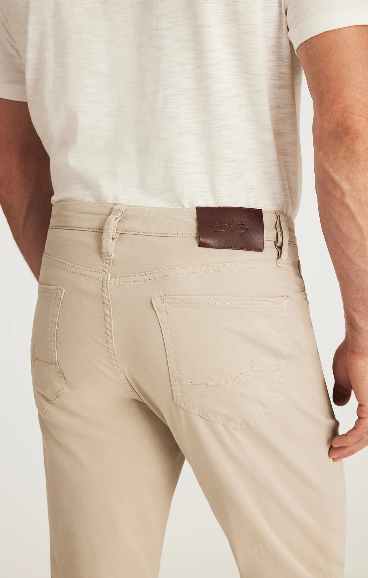 A man with light brown hair and a beard wears a tan blazer, brown sweater, white collared shirt, 34 HERITAGE - CHARISMA RELAXED STRAIGHT LEG PANT IN DAWN TWILL by 34 HERITAGE, and brown shoes against a plain white background.