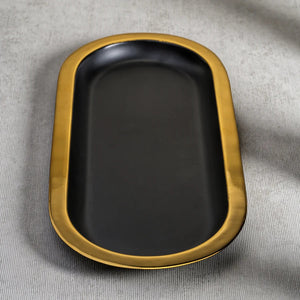The ZODAX OVAL TRAY - BLACK WITH GOLD BORDER is a modern serving tray with a matte black oval base and a bold gold rim, shown elegantly on a white background.
