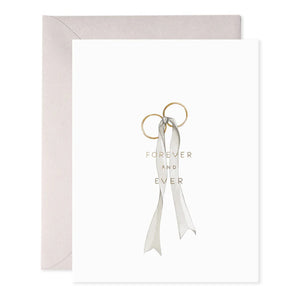 The E. FRANCES PAPER Wedding Rings Greeting Card showcases two intertwined gold rings tied with a gray ribbon and elegant foil accents, inscribed with "FOREVER AND EVER." A handcrafted watercolor touch enhances the card, complemented by a beige envelope.