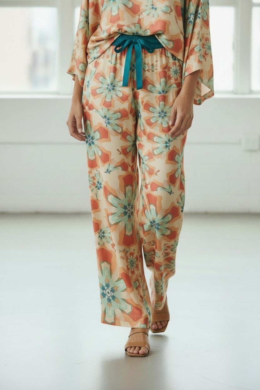 FRANCO FERRARI's ALOE SILK TROUSER is high-waisted with a wide-leg cut, showcasing a resort-style floral print in vibrant orange, teal, and pink on a light background with large blossoms for an eye-catching look.