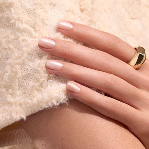 Wearing a black satin top, a person holds a bottle of MANUCURIST - GREEN™ NAIL POLISH IN PEARLESCENT by MANUCURIST INC, displaying their neatly manicured nails.
