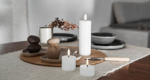 An UYUNI - IVORY PILLAR CANDLE 2X3 by PIFFANY, featuring a visible flame and crafted from high-quality virgin wax, stands upright against a plain white background.