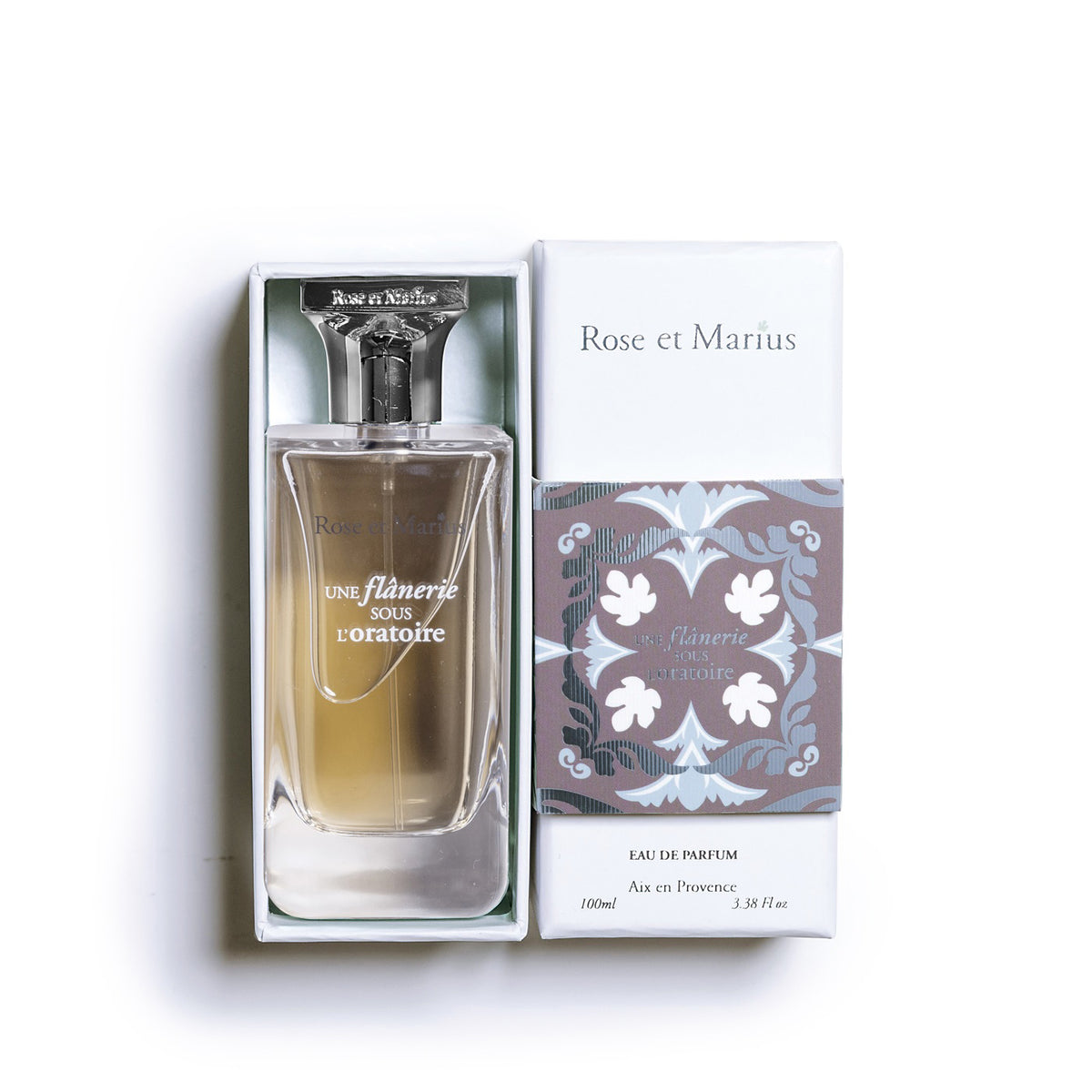 A clear glass ROSE ET MARIUS bottle, labeled &quot;A STROLL UNDER THE ORATORY EAU DE PARFUM 100 ML,&quot; features a silver spray top, square cap, and a &quot;Unisexe&quot; label—capturing the floral essence of this unisex fragrance.