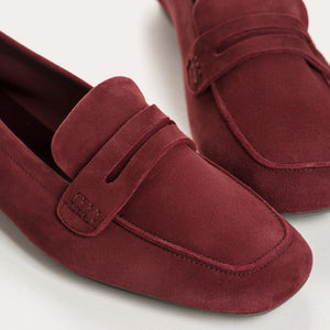 Close-up of the REQINS - HEMA SUEDE LOAFER IN BORDEAUX by REQINS, showcasing artisanal craftsmanship with burgundy suede, detailed stitching, a front strap, and a soft leather insole, displayed on a light surface.