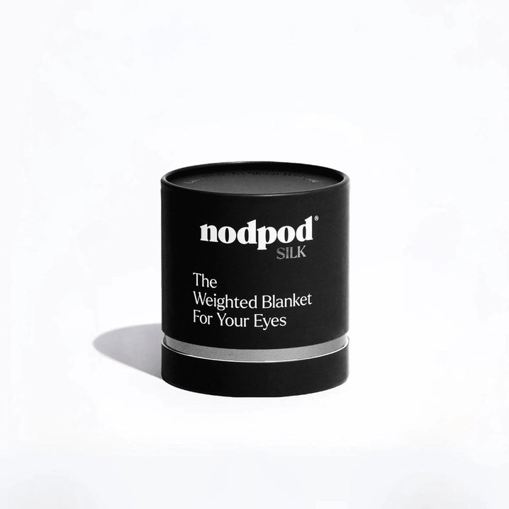The NODPOD Silk Weighted Sleep Eye Mask in Noir by NODPOD is a dark blue, segmented eye mask featuring a strap-free design and unique four-pad shape. Text highlights its calming effect for stress relief and relaxation, all set against a light background.