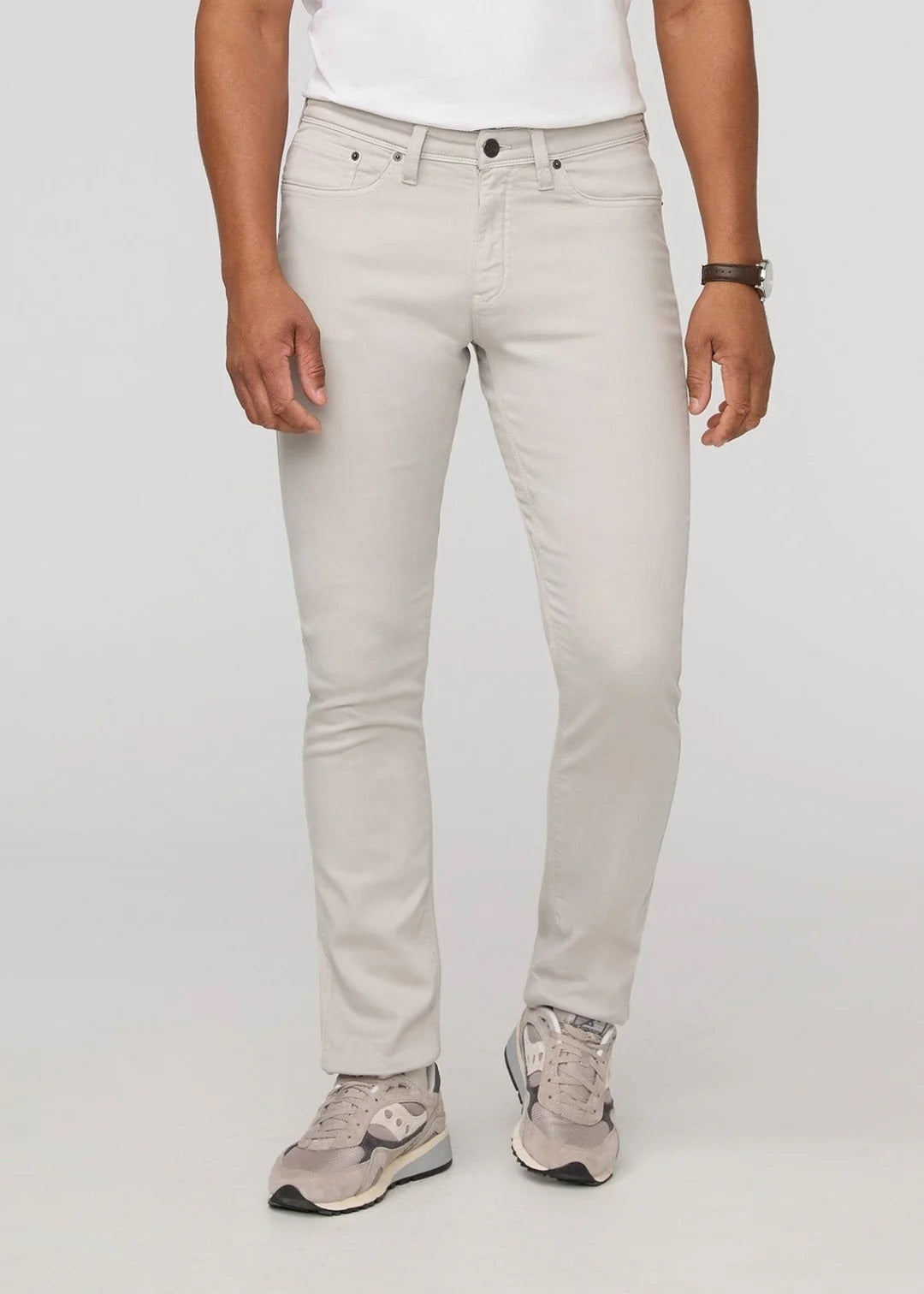 A person stands facing forward on a plain light background, wearing DUER NO SWEAT ATHLETIC TAPER PANTS IN MIST and matching light gray sneakers, feet slightly apart.