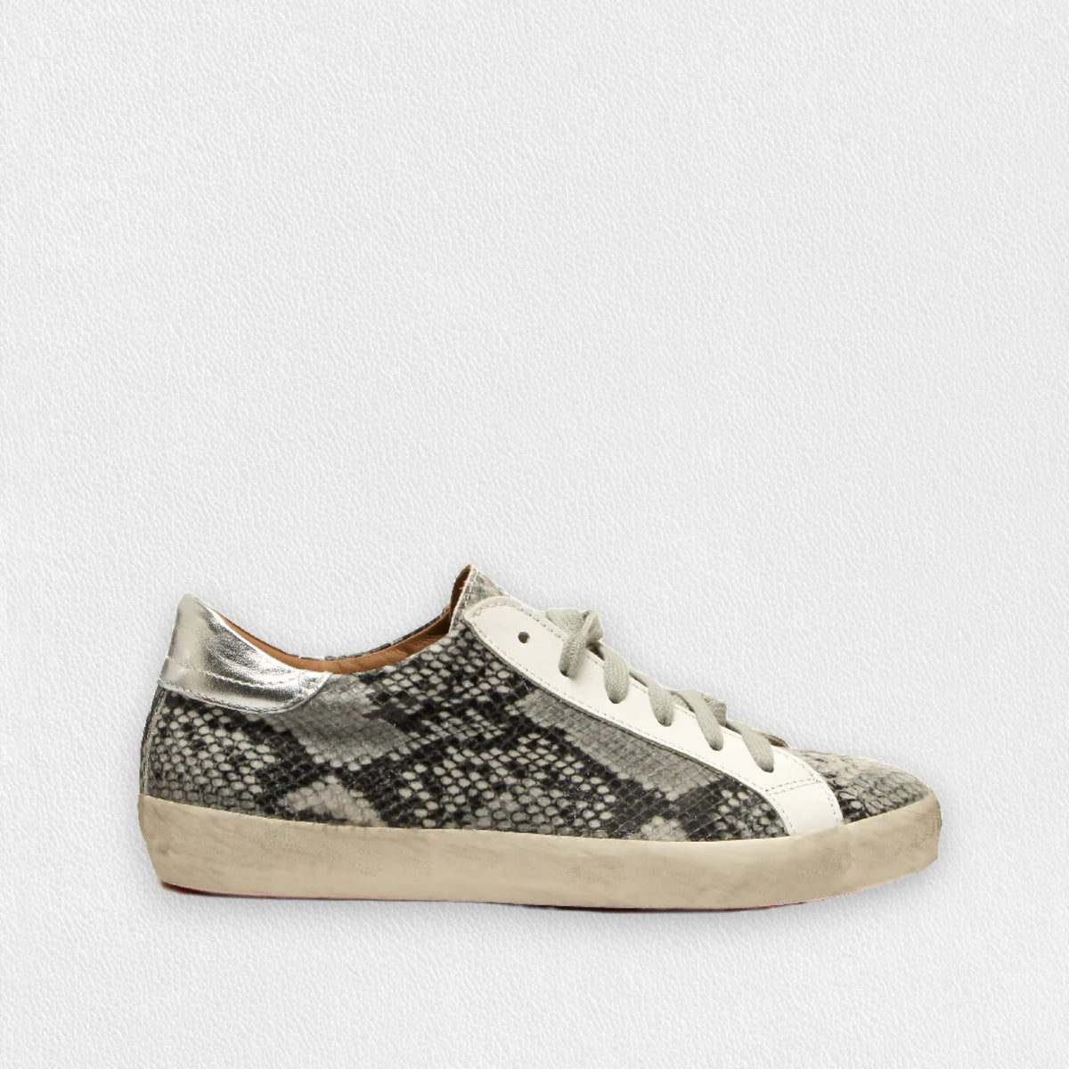 The MICHELE LOPRIORE - GEMMA SNEAKER IN PYTHON PRINT is a low-top shoe with an off-white extra light rubber sole and a grey and white snakeskin pattern in printed leather. It features white laces, a sleek white stripe along the side, and a metallic silver heel cap for added shine against a plain light grey background.