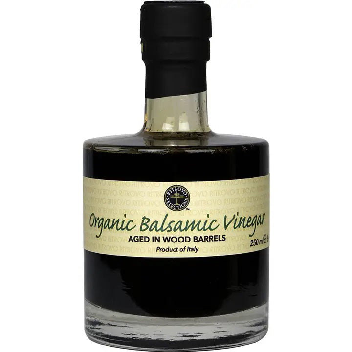 A bottle of USDA Certified Organic Balsamic Vinegar from RITROVO, aged in wood barrels. The dark brown liquid is contained in a clear, short bottle with a black cap, and a beige label displays information, including "250 mL" and "Made in Italy.