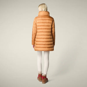A woman in the SAVE THE DUCK - LYDIA PUFFER COAT by SAVE THE DUCK, paired with a white dress, maroon knee-high boots, and holding a fluffy light pink clutch, stands against a plain beige background.