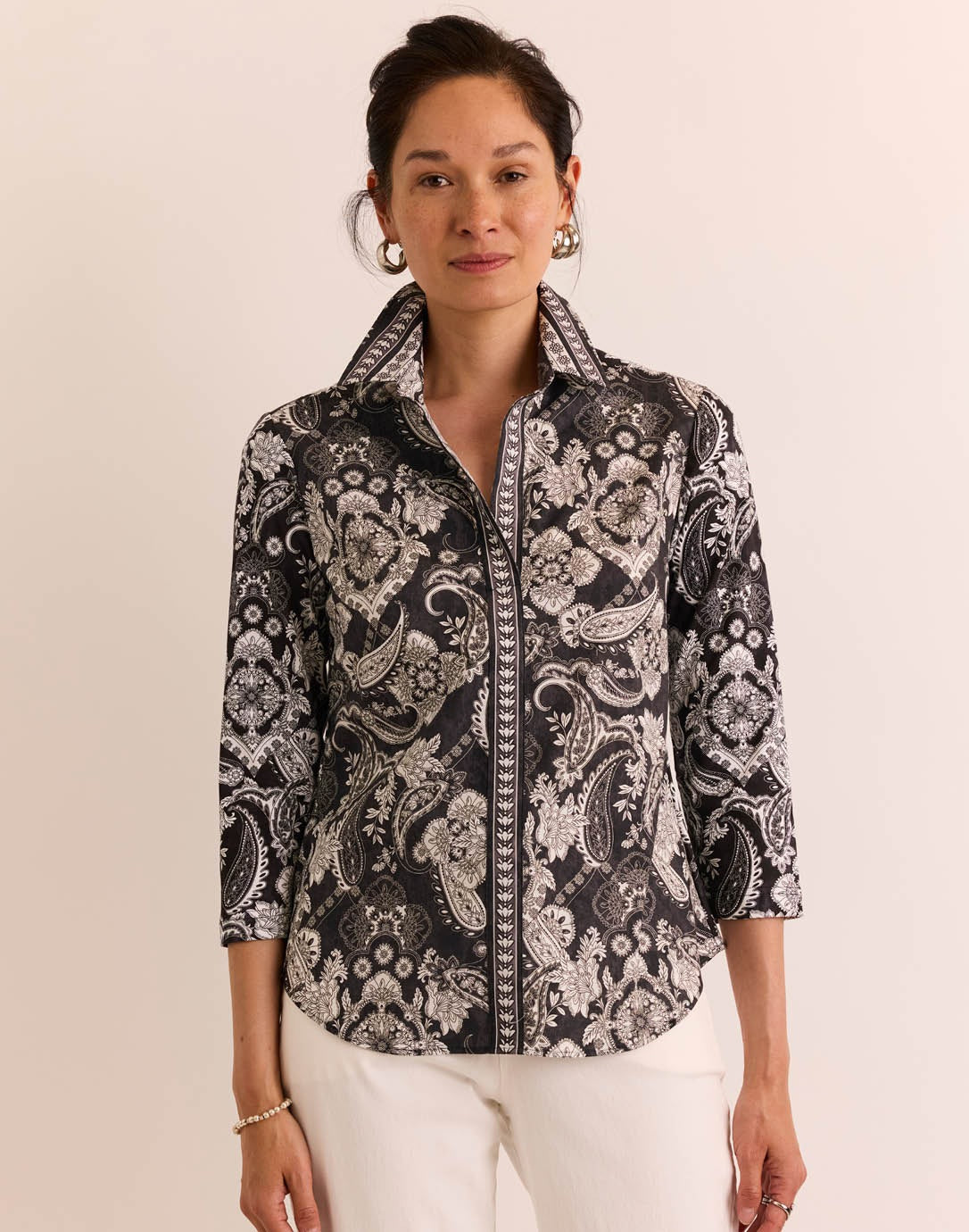 A woman wearing the HINSON WU Lizette 3/4 Sleeve Paisley Print Shirt—a black and white paisley-patterned cotton shirt with a collar—paired with white pants, stands against a plain light background.