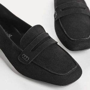 The REQINS HEMA Suede Loafer in Noir features a classic black silhouette, low heel, leather insole, and decorative front strap, shown against a plain light background.