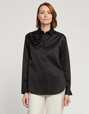A person with short, brown hair is standing and facing away from the camera, wearing a HINSON WU - HALSEY LONG SLEEVE COTTON SATIN SHIRT WITH FLOWER. They have paired this black button-up shirt, made of a cotton and spandex blend, with light-colored pants. The background is plain and light-colored.