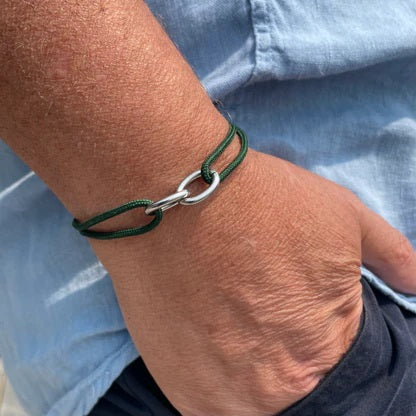 A hand wears the STOLEN RICHES Braga String Bracelet with Linked Chain in green, shown against a light blue shirt and dark pants.