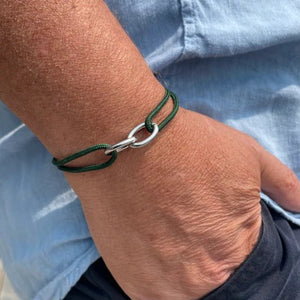 A hand wears the STOLEN RICHES Braga String Bracelet with Linked Chain in green, shown against a light blue shirt and dark pants.