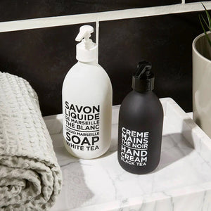 A sleek pump bottle of CIE LUXE BRANDS' COMPAGNIE DE PROVENCE - BLACK TEA HAND CREAM is infused with nourishing shea butter. The elegant white label displays "CREME MAINS LE NOIR HAND CREAM BLACK TEA" in French and English, offering a luxurious touch for your hands.