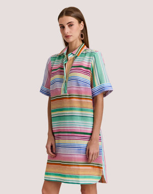 A woman wears the HINSON WU AILEEN Short Sleeve Linen Dress in Multi Stripe, a knee-length design with colorful stripes, a collar, front buttons, and pockets.