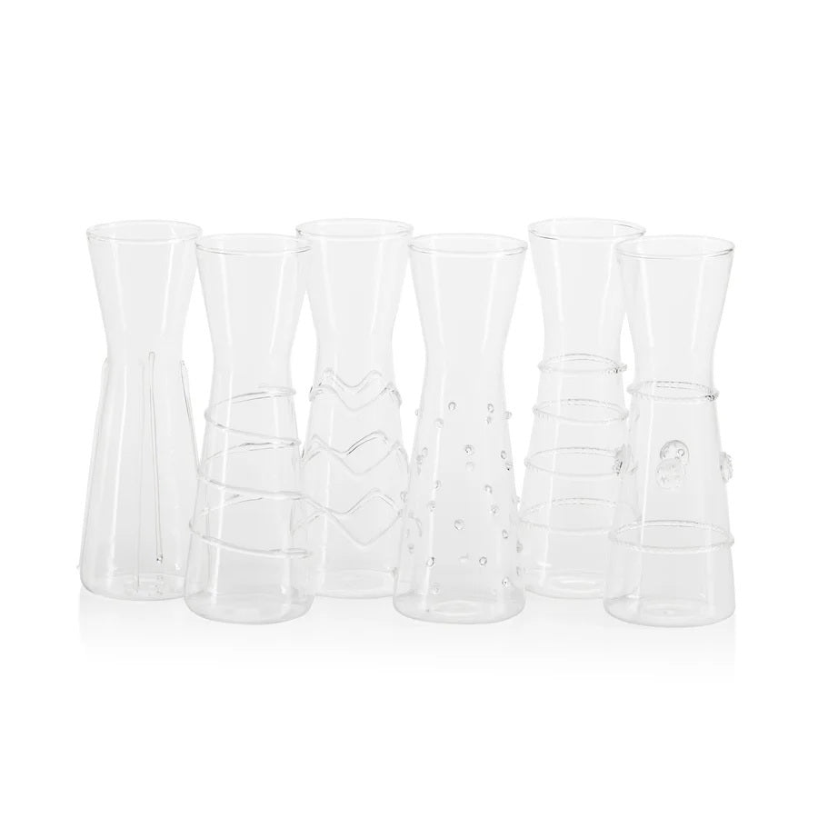 Six ZALLI SINGLE SERVE GLASS CARAFES by ZODAX, each featuring a unique etched design, are arranged on a reflective silver tray with a blurred green background.