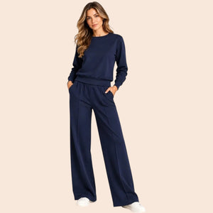 A woman wears a SOFTIES - DREAMTECH BOAT NECK WITH PINTUCK PANT SET in olive green, featuring a long-sleeve boat neck top and matching wide-leg pintuck pants.