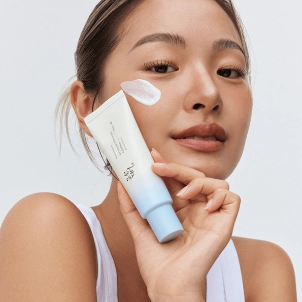 A tube of KOSMIC KBEAUTY SKINCARE BEAUTY OF JOSEON - RELIEF SUN SUNSCREEN, AQUA FRESH SPF 50+ is positioned on and next to four ice cubes containing embedded flowers, set against a crisp white background.