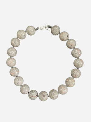 The ANN LIGHTFOOT Fossil Coral Ras du Cou Necklace features large, polished round fossil coral beads in light gray and beige with circular patterns and a sterling silver clasp, shown on a dark gray background.