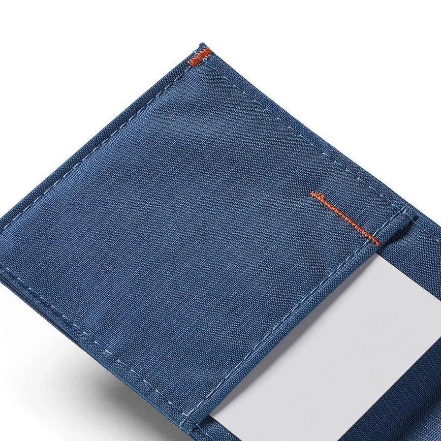 The ALLETT Sport Wallet in RFID-blocking indigo blue nylon features a minimalist design with an orange triangular logo on the corner, shown against a white background.