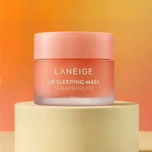 A jar of KOSMIC KBEAUTY SKINCARE’s LANEIGE - LIP SLEEPING MASK in Grapefruit rests on a beige pedestal against a warm orange and yellow gradient background, showcasing this nourishing overnight lip treatment.