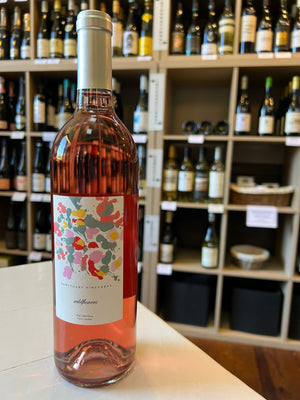 Enjoy a bottle of SANCTUARY 'WILDFLOWERS' ROSÉ by WINE: FREEDOM BEVERAGE—light pink with a white label featuring colorful abstract flowers and a gold foil cap, perfect for experiencing North Carolina's unique wine flavors.