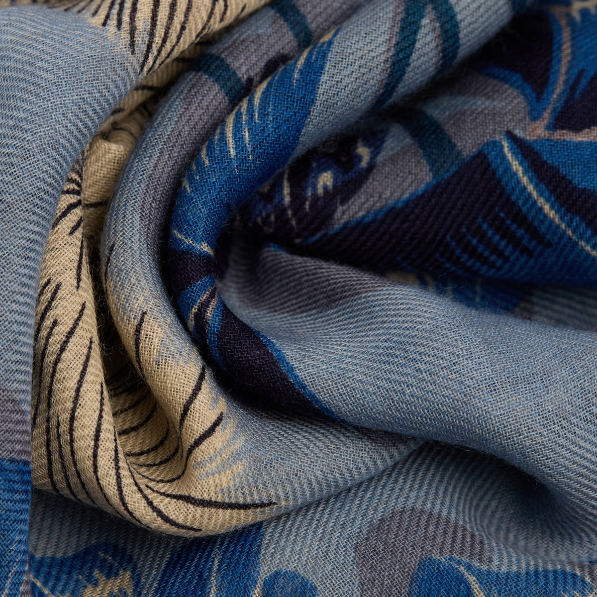 A close-up of the INOUI EDITIONS TOUTOU DOGGIE Wool Scarf in Blue shows its soft, woven texture and abstract blue, beige, and navy patterns. This 70x70cm INOUI accessory is gently twisted to highlight its intricate design—perfect for any wardrobe.