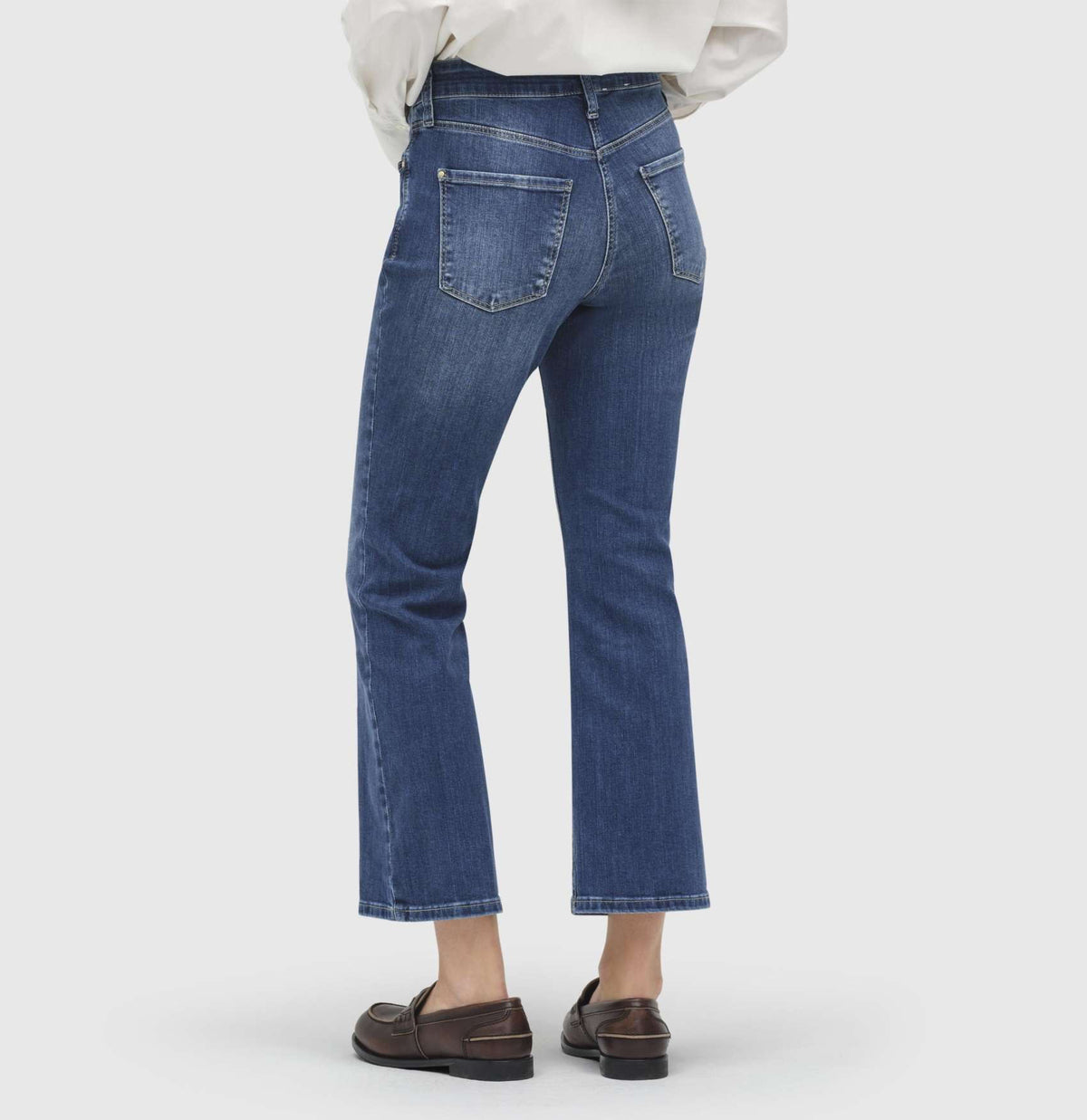 A person is standing against a plain white background, wearing MAC JEANS - DREAM KICK OUTWORN BLUE and white sneakers. The jeans are slightly flared at the bottom and feature typical denim stitching. The upper body of the person is not fully visible, but they appear to be wearing a white top.