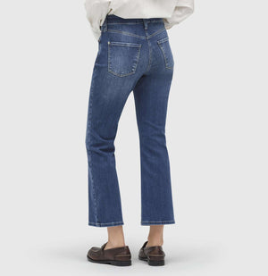 A person is standing against a plain white background, wearing MAC JEANS - DREAM KICK OUTWORN BLUE and white sneakers. The jeans are slightly flared at the bottom and feature typical denim stitching. The upper body of the person is not fully visible, but they appear to be wearing a white top.