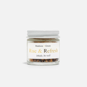 A small glass jar with a white screw-on lid labeled "MADISON GREEN - ROSE AND REFRESH MORNING AROMATHERAPY INHALER," containing mixed dried botanicals for natural stress relief, sits against a plain white background.